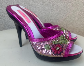 May include: A pair of pink high-heeled shoes with a floral design and sequins. The shoes have a white platform and a black heel.