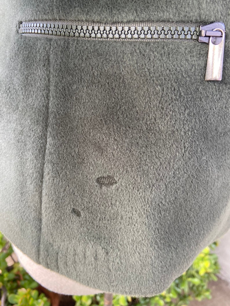 May include: A dark green jacket with a zipper closure. The jacket has a small hole in the fabric.
