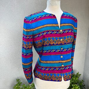 May include: A long-sleeved, button-up blouse with a colorful striped pattern. The pattern features blue, turquoise, pink, gold, and purple stripes with a repeating design of gold chains and jeweled pendants.
