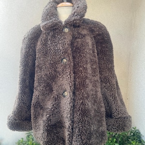 May include: A brown faux fur jacket with a button closure and a collar. The jacket is on a mannequin.