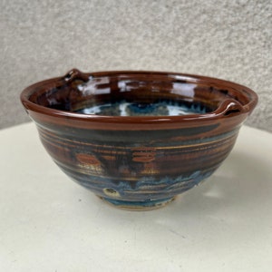 以下が含まれることがあります： 青と白の釉薬がかかった茶色の陶器のボウル。ボウルは、縁の周りにわずかな縁があり、底に排水穴があるユニークなデザインです。