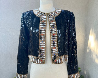 May include: A black sequined jacket with gold and pearl embellishments. The jacket has a front closure and long sleeves.
