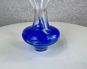 Puede incluir: Un jarrón de vidrio azul y blanco con un diseño de espiral. El jarrón tiene un cuello de vidrio transparente y una base redonda.