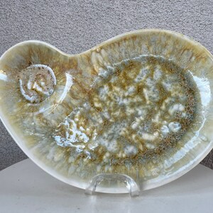 May include: A white ceramic serving dish with a unique, organic shape and a speckled, brown and grey glaze.