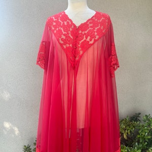 May include: A vintage red sheer nightgown with a floral lace collar, sleeves, and hem. The nightgown is displayed on a mannequin, showcasing its flowing, lightweight design. The lace detailing and button closure add a touch of elegance.