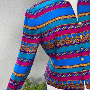 May include: A long-sleeved blouse with a colorful striped pattern featuring gold chains, turquoise, pink, and blue. The blouse has a V-neck and button closure.