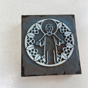 May include: A vintage woodblock stamp with a blue and white design of a person standing in a circle of flowers.