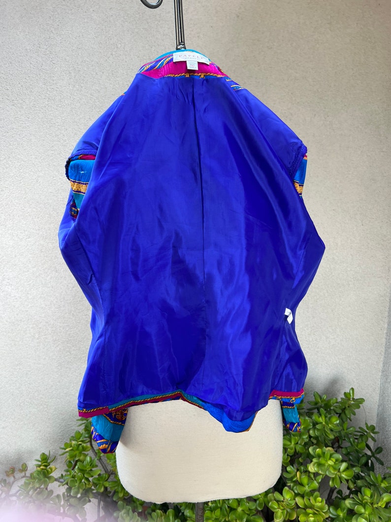 May include: A blue, pink, and gold patterned blazer with a blue satin lining. The blazer has a collar and a button closure. The label on the blazer reads "Bakeman".