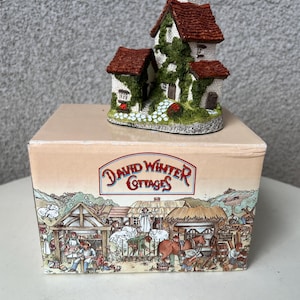 May include: A miniature cottage with a green ivy covered exterior and a red tiled roof. The cottage is sitting on a box with the text "David Winter Cottages" printed on it.