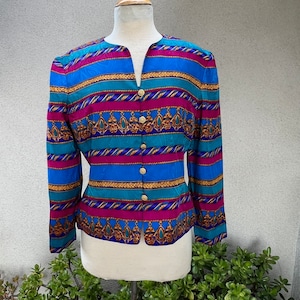 May include: A long-sleeved, button-up blouse with a colorful striped pattern. The fabric features a geometric design with gold accents. The blouse has a V-neck and a fitted silhouette.