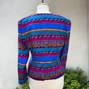 May include: A blue, pink, and gold striped blouse with a patterned design. The blouse has long sleeves and a v-neck.