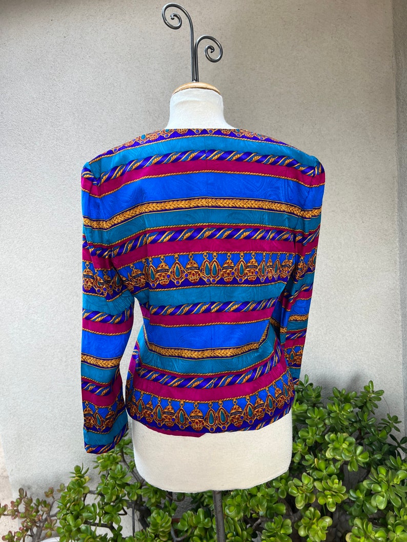 May include: A blue, pink, and gold striped blouse with a patterned design. The blouse has long sleeves and a v-neck.