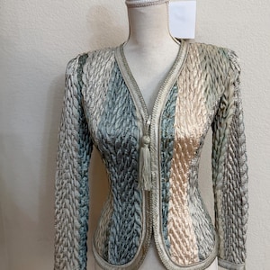 May include: A textured jacket with a V-neck and long sleeves. The jacket features a zipper closure with a tassel and is displayed on a mannequin. The color palette includes shades of blue, beige, and gray.