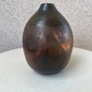Può includere: Un piccolo vaso in ceramica verde scuro con una glassa di rame. Il vaso ha un corpo arrotondato e un collo stretto.