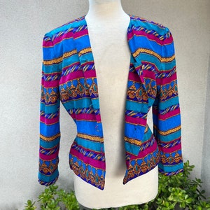 May include: A blue, pink, and gold striped blazer with a geometric pattern. The blazer has a long sleeve and a button closure.