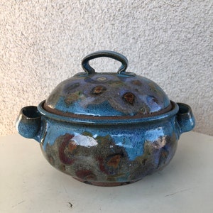 Könnte beinhalten: Eine blaue und braune Keramik-Auflaufform mit Deckel und zwei Griffen. Die Form hat eine gesprenkelte Glasur und einen rustikalen Look.