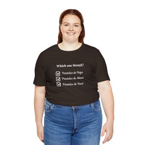 May include: A dark brown t-shirt featuring the question "Which one though?" above a white checklist. The checklist includes three options: Pasteles de Hoja, Pasteles de Masa, and Pasteles de Yuca.