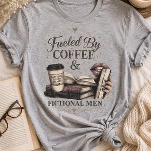 May include: A heather gray t-shirt featuring the text "Fueled By Coffee & Fictional Men." The graphic includes a coffee cup, books, and lips holding a book. The shirt is knotted at the bottom.