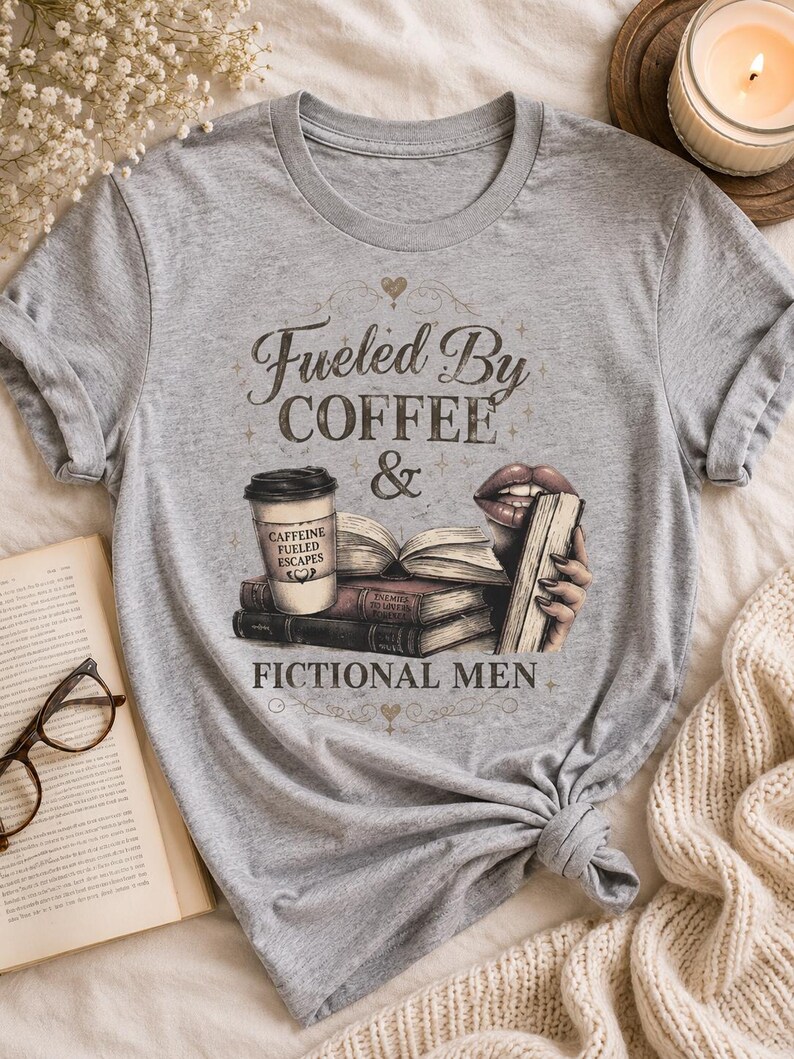 May include: A heather gray t-shirt featuring the text "Fueled By Coffee & Fictional Men." The graphic includes a coffee cup, books, and lips holding a book. The shirt is knotted at the bottom.
