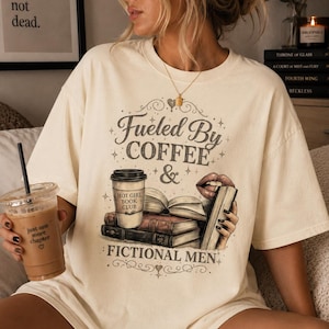 May include: Cream-colored t-shirt with the text "Fueled By Coffee & Fictional Men." The graphic includes a coffee cup, books, and lips. The shirt also has the text "Hot Girl Book Club."