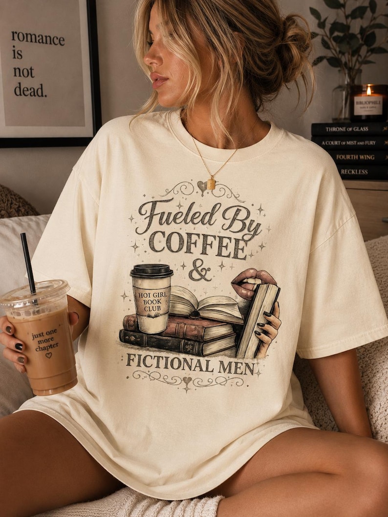 May include: Cream-colored t-shirt with the text "Fueled By Coffee & Fictional Men." The graphic includes a coffee cup, books, and lips. The shirt also has the text "Hot Girl Book Club."