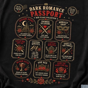 May include: A black t-shirt featuring a graphic design titled Dark Romance Passport. The print includes eleven rectangular frames with red and gold text and illustrations such as a castle, swords, a mask, binoculars, a cage, a dagger, a goblet, and a bed.