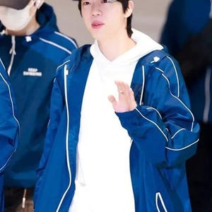 May include: A person wearing a gray baseball cap with a white design, a white hoodie, and a blue jacket with white trim. The person is also wearing blue jeans.