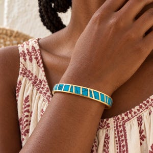May include: A gold-toned cuff bracelet featuring inlaid segments of bright turquoise stone. The bracelet has a smooth, polished metal frame that separates the individual rectangular pieces of blue stone, creating a geometric pattern around the wrist.
