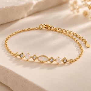 May include: A gold chain bracelet featuring a central marquise-cut opal, flanked by two round opals and four small square-set clear stones. The delicate link chain includes a circular clasp and an adjustable extension with a small flat charm.
