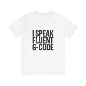 May include: White t-shirt with the text "I SPEAK FLUENT G-CODE" in black block letters. The shirt is a short-sleeved crew neck style, suitable for casual wear. The text is centered on the front of the shirt.