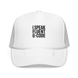 Könnte beinhalten: Eine weiße Trucker-Cap mit einem Netzrücken und einer festen Vorderseite. Auf der Vorderseite steht der schwarze Text "I SPEAK FLUENT G-CODE" in einer fetten, serifenlosen Schrift. Die Kappe hat eine strukturierte Krone und einen gebogenen Schirm.