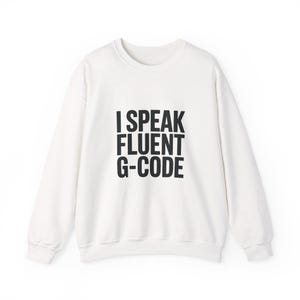 May include: A white sweatshirt with the text "I SPEAK FLUENT G-CODE" in bold black letters. The crew neck sweatshirt is a casual style, suitable for everyday wear. The text is centered on the front of the garment.