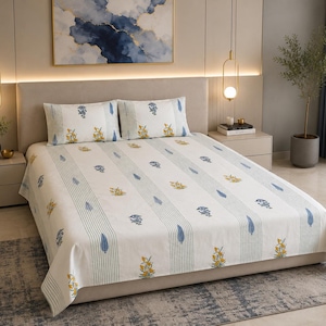 Op de afbeelding: Een wit laken en twee bijpassende kussenslopen met een patroon van verticale groene strepen afgewisseld met kleine blauwe en gele bloemmotieven. De beddengoedset ligt over een bed en toont een strak en gecoördineerd ontwerp.