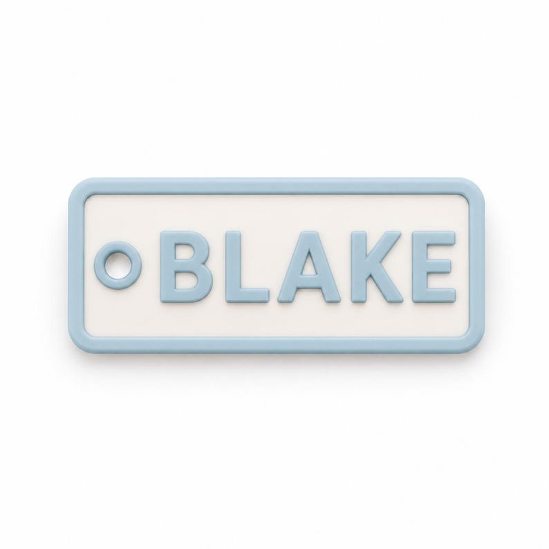 May include: A rectangular name tag with rounded corners. The tag has a light blue border and the name "BLAKE" in light blue, raised letters. The background is white. The tag is a simple, clean design.
