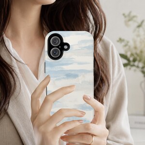 May include: A smartphone case featuring a soft watercolour design with horizontal brushstrokes in shades of light blue and white. The case has a black camera module cutout at the top left corner, designed to accommodate two circular camera lenses.