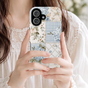 Könnte beinhalten: Eine rechteckige Smartphone-Hülle mit einem Patchwork-Design aus hellblauen und cremefarbenen Blumenmustern, Karomustern und einer gesteppten Textur. Die Hülle hat ein schwarzes Kameragehäuse mit zwei runden Linsen und einem kleinen Blitz.