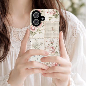 May include: A smartphone case featuring a patchwork design of cream-colored squares. The pattern includes illustrations of pink roses, green leaves, small blue flowers, and a beige checkered print, all arranged in a grid with visible stitching details.