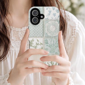Puede incluir: Una funda para smartphone con un diseño de patchwork en tonos verde salvia y blanco. El patrón incluye secciones de lunares, motivos florales, ilustraciones botánicas y un detalle de bordado circular tipo encaje sobre un fondo texturizado.