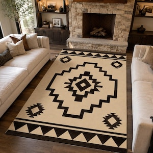 May include: A rectangular area rug featuring a cream-colored base with a bold black geometric pattern. The design includes a large central diamond motif, smaller diamond accents in the corners, and a repeating triangular border along the edges.