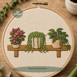 Puede incluir: Un bastidor de bordado circular de madera que contiene un panel de tela con un diseño bordado de tres plantas en macetas sobre un estante. Las plantas incluyen una planta con flores rosas, una planta rosario colgante y una costilla de Adán. Texto: PDF Download.