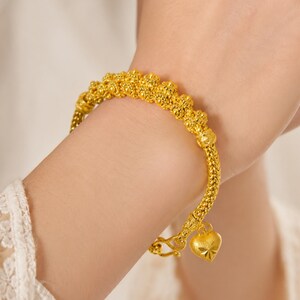 Pode incluir: Uma pulseira de ouro com um design de corrente de contas texturizada e acabamento polido. A pulseira inclui um pequeno pingente em forma de coração com uma gravação de estrela e um fecho de gancho, num tom de ouro amarelo brilhante.