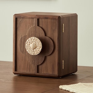 May include: A wooden cabinet with a dark brown finish. The cabinet has two doors with a decorative floral design and a textured, gold-colored circular handle. The hinges are gold-colored. The cabinet is on a wooden surface.