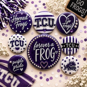 May include: A collection of eight circular pin-back buttons featuring purple and white designs with TCU branding. Text includes Horned Frogs, Go Frogs, forever a FROG, and purple pride. Some buttons feature polka dots, stripes, and small heart accents.