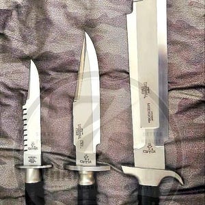 Könnte beinhalten: Drei silberfarbene Messer mit schwarz umwickelten Griffen, nach Größe angeordnet. Das kleinste Messer hat einen gezackten Rücken. Jede Klinge ist mit Text graviert, einschließlich des Wortes CAYIN. Die Messer haben Metallparierstangen und Knäufe.