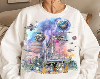 May include: A white long-sleeve sweatshirt featuring a colorful graphic print of a castle, space ships, planets, and cartoon characters. The design includes a vibrant watercolor-style background with shades of blue, purple, and orange.