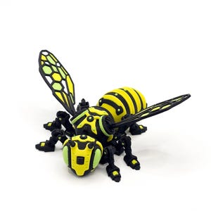 May include: A 3D-printed model of a mechanical bee. The bee features a yellow and black striped abdomen, yellow head and green accents. The wings are yellow and black. The legs and other mechanical parts are black.