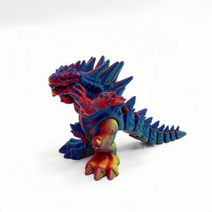 Könnte beinhalten: Eine mehrfarbige Monsterfigur mit einem Farbverlauf in Rot, Blau und Gelb. Die Kreatur hat eine texturierte, schuppige Oberfläche mit markanten Stacheln entlang des Rückens und Schwanzes, einem breiten Maul und krallenartigen Füßen.
