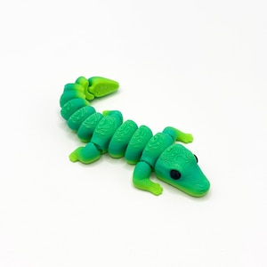 May include: A flexible, articulated lizard figurine featuring a gradient color scheme that transitions from bright lime green to a deeper emerald green. The toy has a segmented body with visible 3D printed layer lines and two small black eyes.