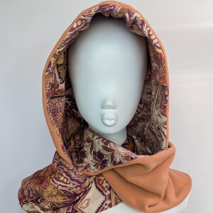 May include: A peach-coloured fleece hood with a patterned interior. The interior fabric features a design in shades of brown, purple, and cream. The hood is displayed on a mannequin head.