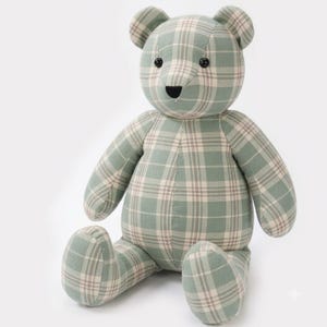 Puede incluir: Un oso de peluche hecho de tela con un patrón de cuadros en color verde salvia y crema. El juguete tiene dos pequeños ojos redondos negros y una nariz negra bordada. Se muestra en posición sentada con los brazos y las piernas extendidos.